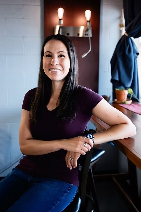 Lauren Moore smiling, seated at a wooden counter with her arms resting on the back of a chair.